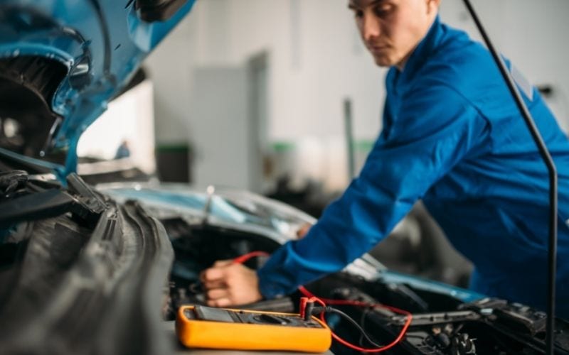 Car repairman with a multimeter for a battery inspection